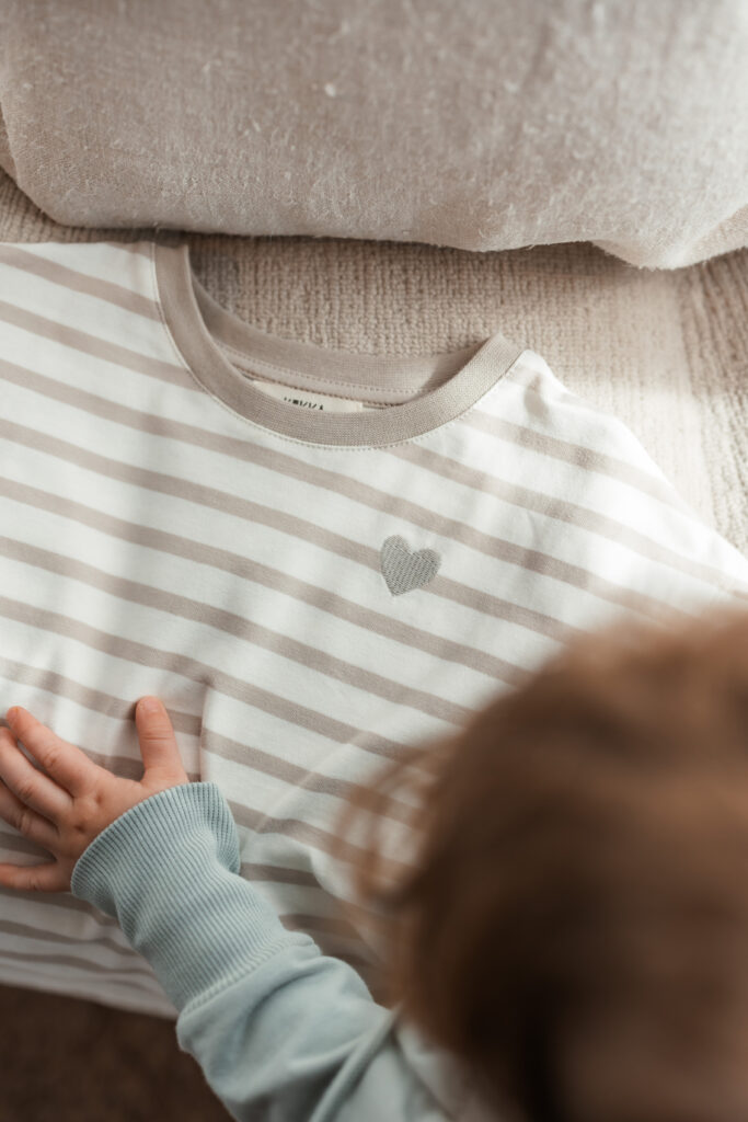 Kleinkind berührt ein T-Shirt mit Herz aus nachhaltiger Kinderkleidung von KUKKA